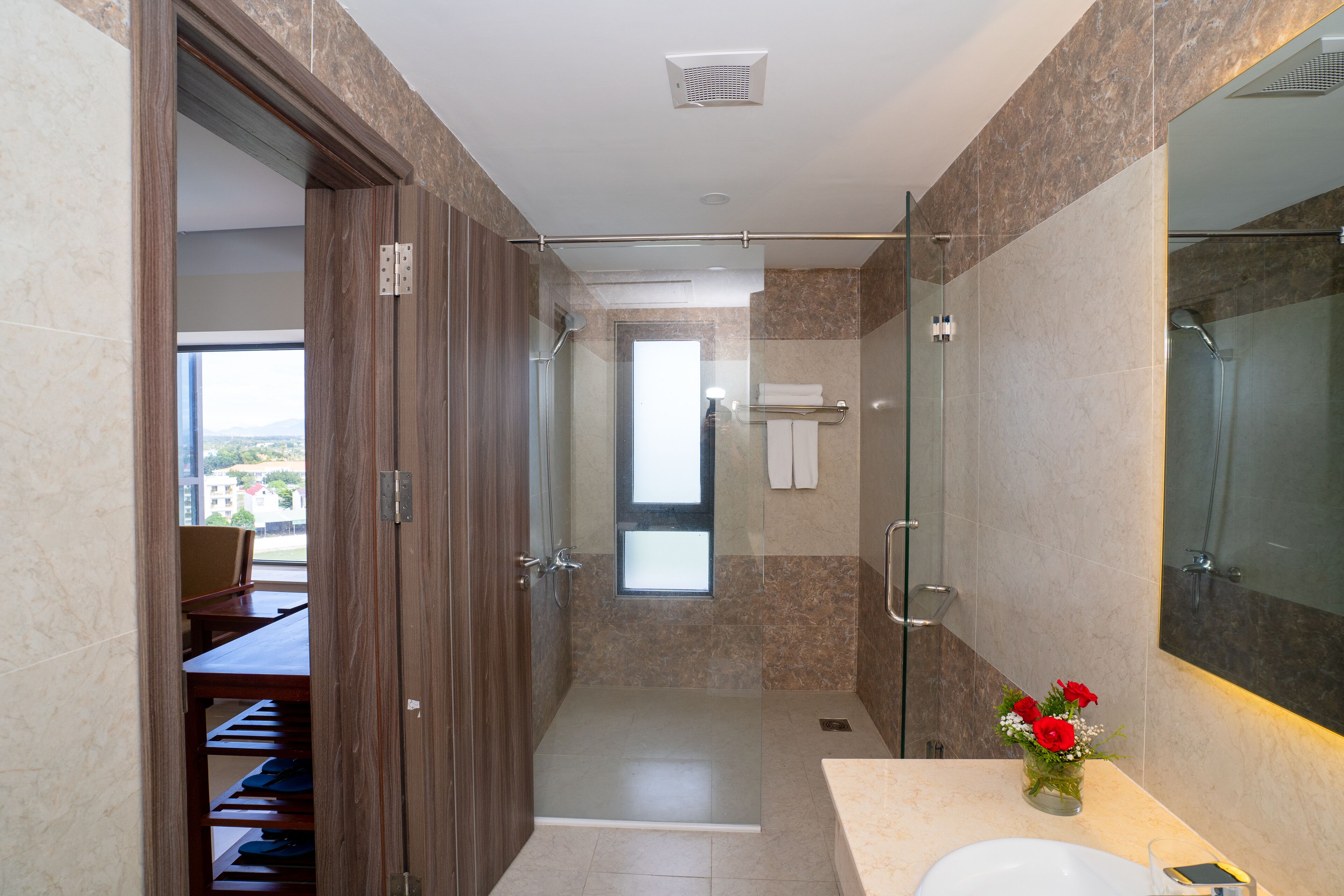 A modern bathroom with a glass-enclosed shower, a vanity with a mirror, and a view of a dining area.