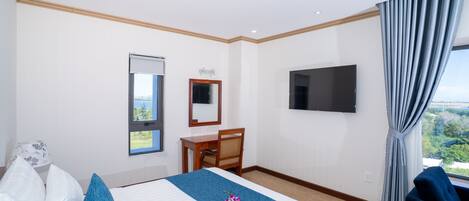 A hotel room with a bed, a desk, a chair, a TV, and a window with curtains.