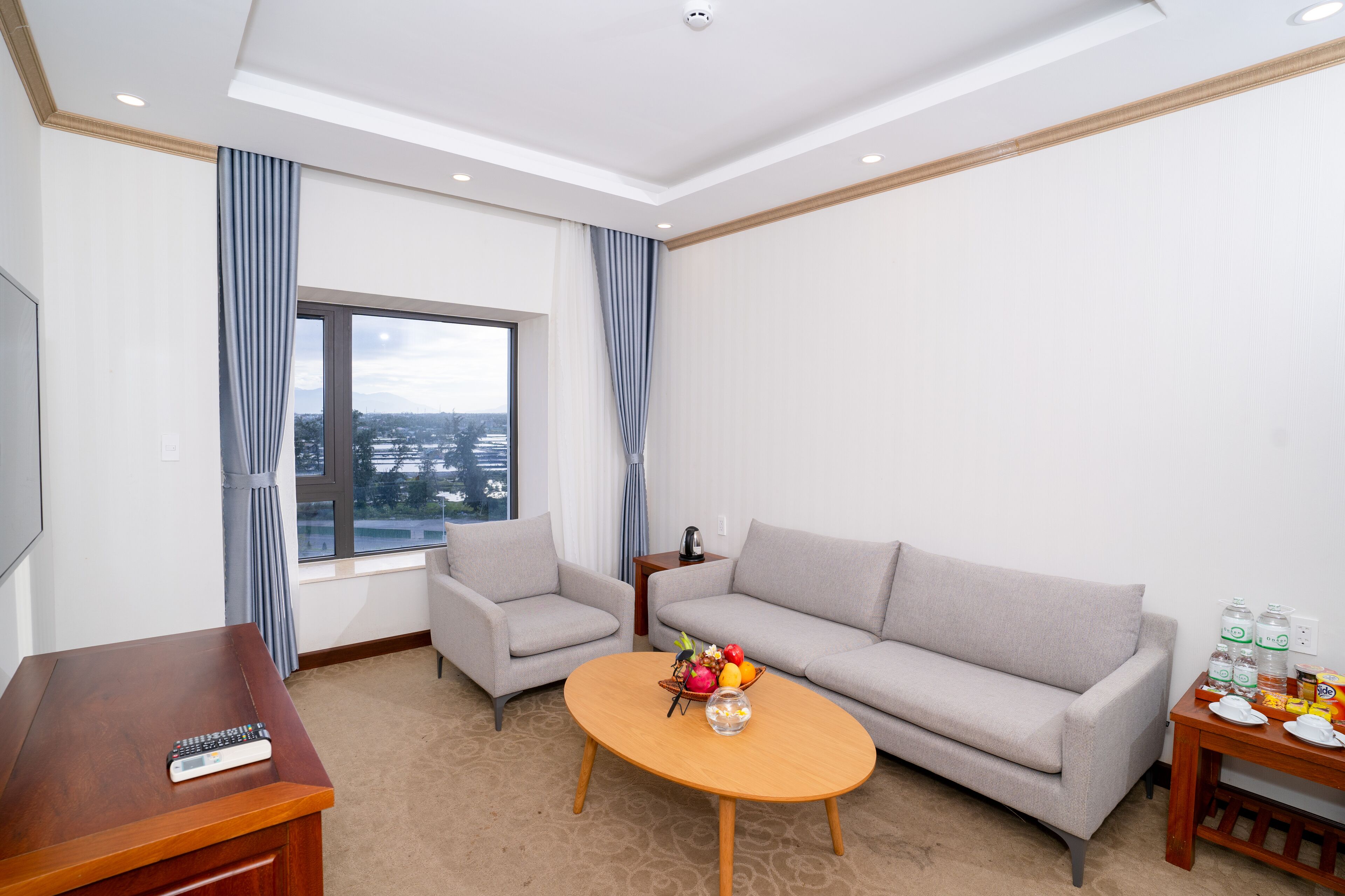 A modern hotel room with a sofa, armchair, and a small table with a fruit bowl.
