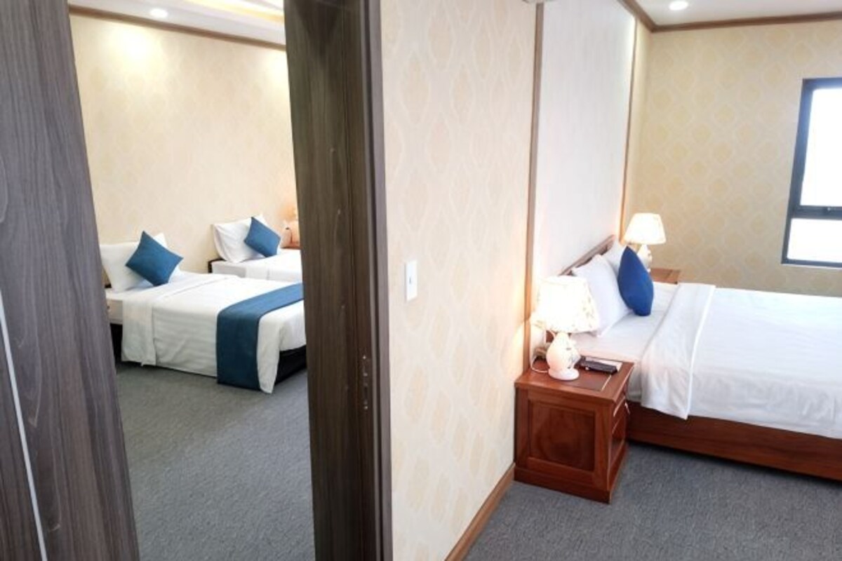 Een hotelkamer met twee bedden, een houten nachtkastje, een lamp en een raam.