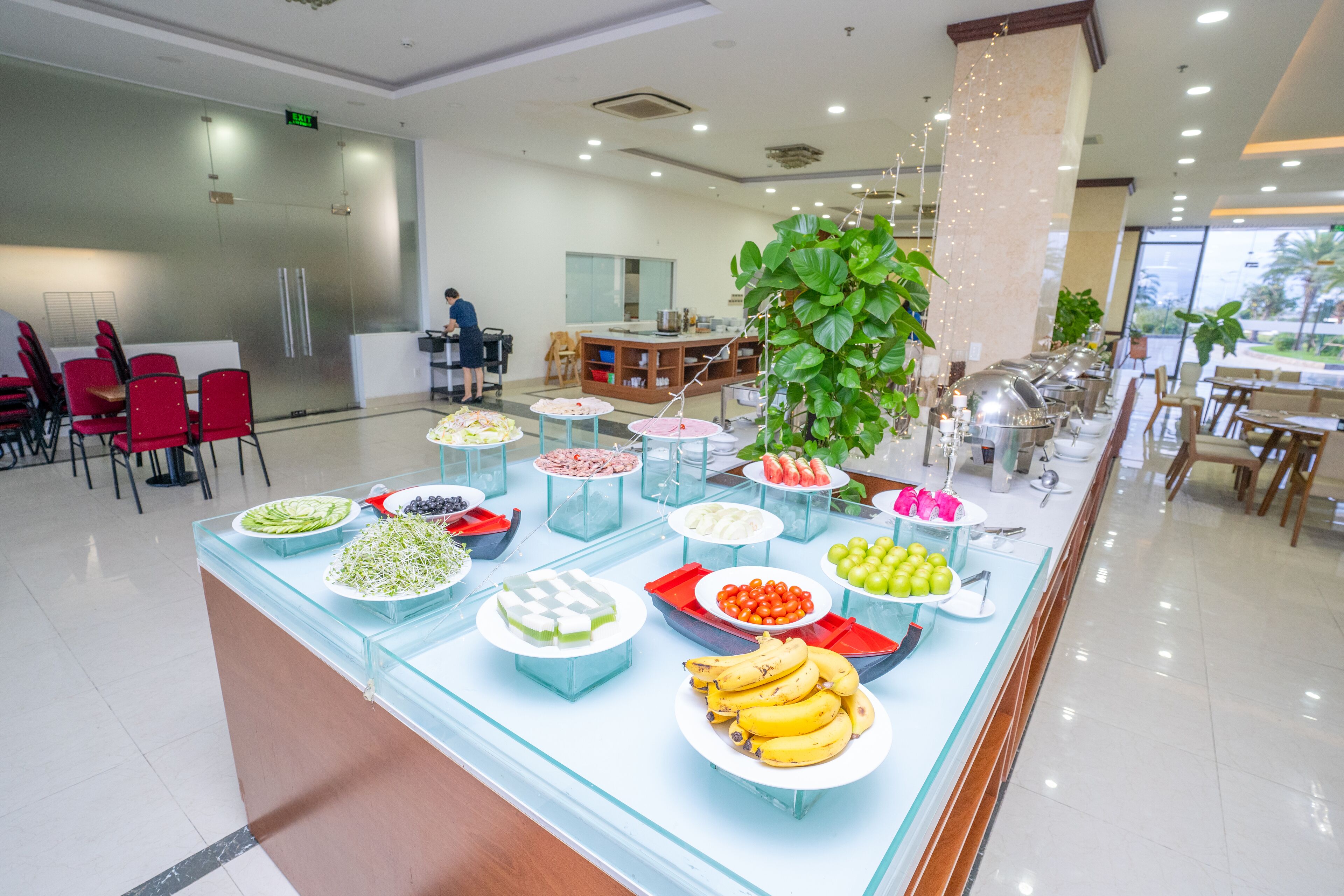 A buffet with various food items and a seating area with red chairs and tables.