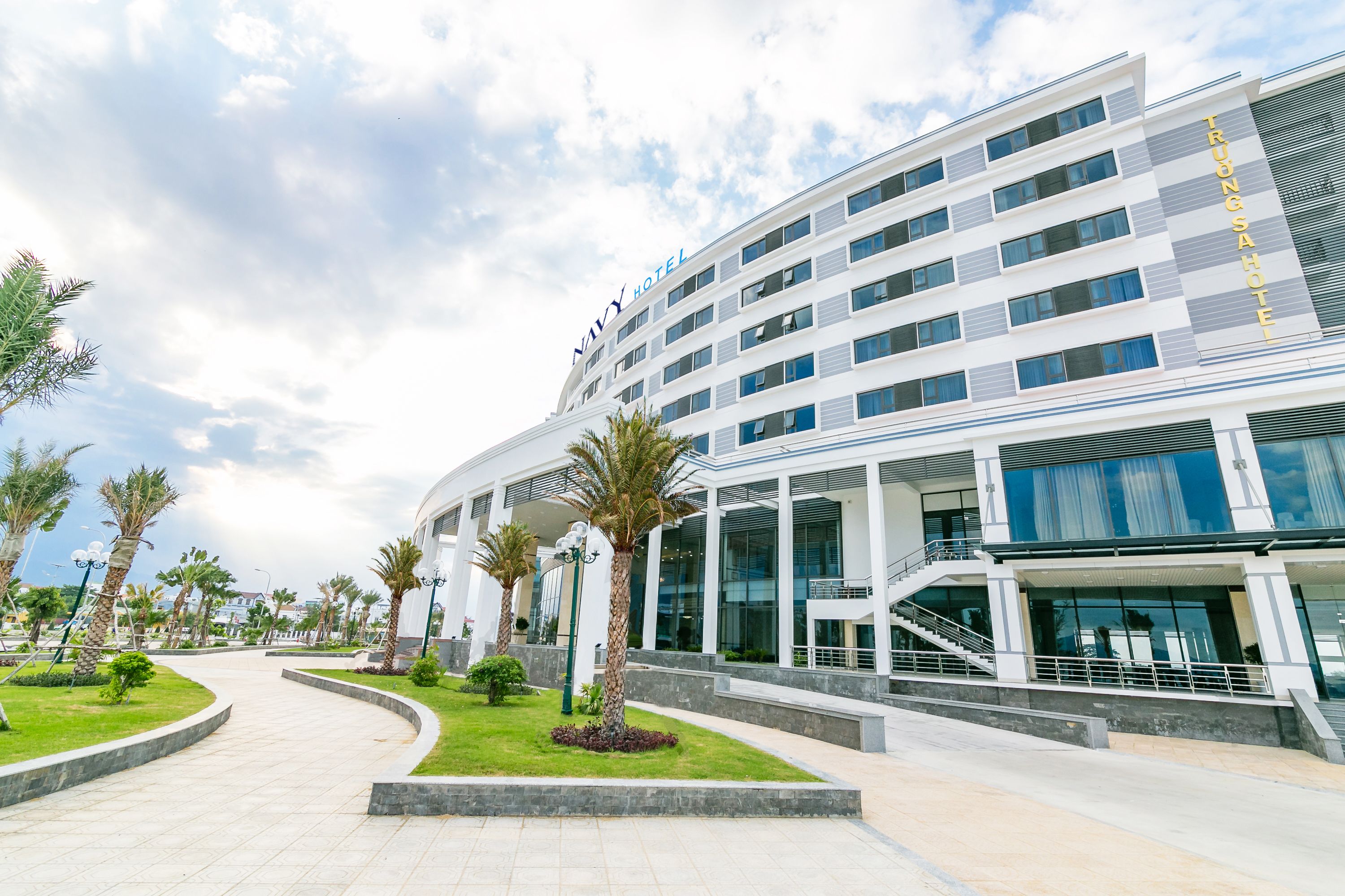A modern hotel with a curved facade, multiple floors, and a well-maintained outdoor area with palm trees and a landscaped garden.