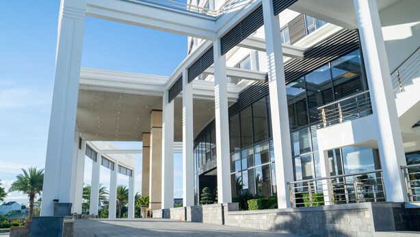 Un edifici modern amb entrada coberta, grans finestres i un cel clar.