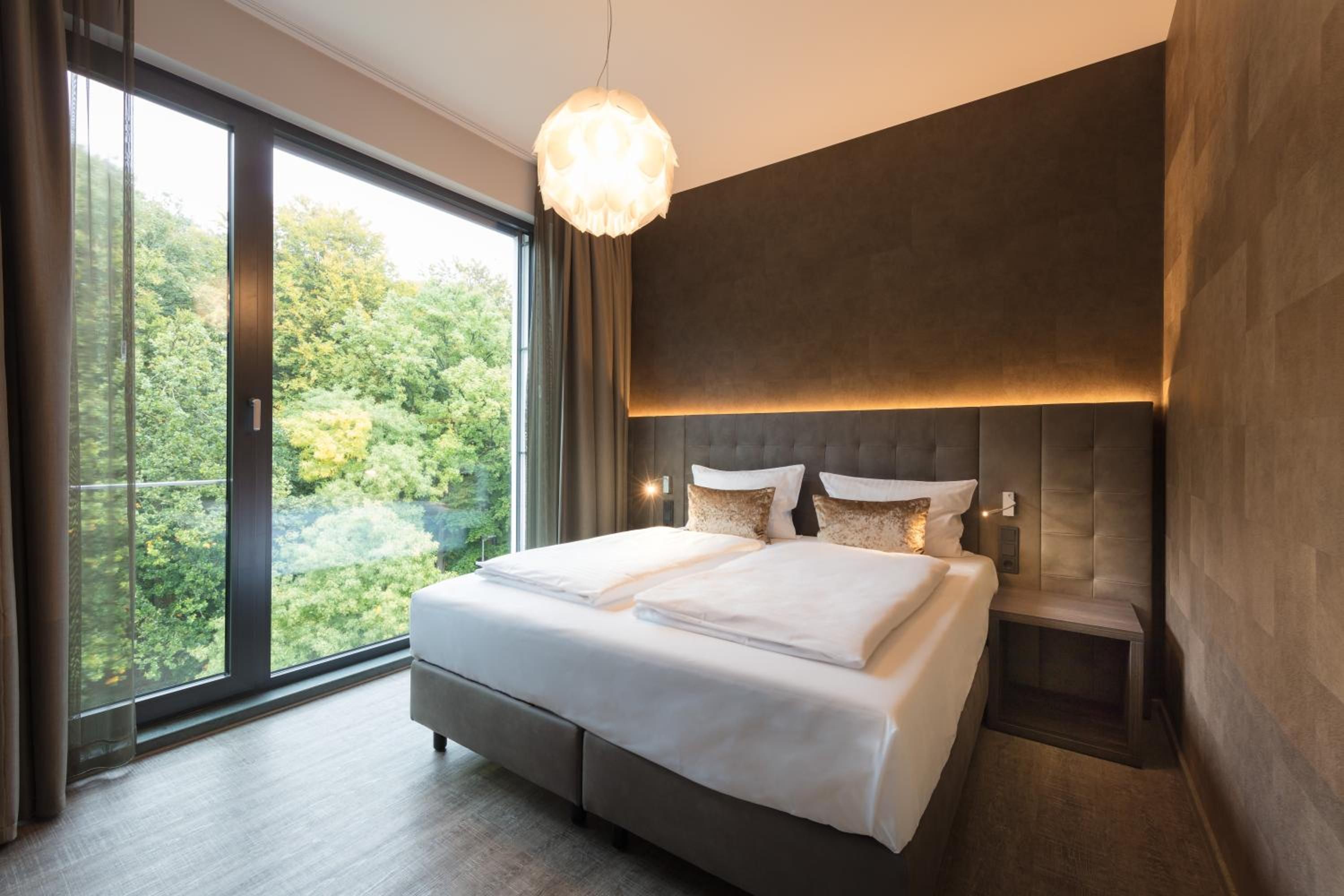 Un dormitorio moderno con una cama grande, una mesita de noche y vistas a zonas verdes a través del ventanal.