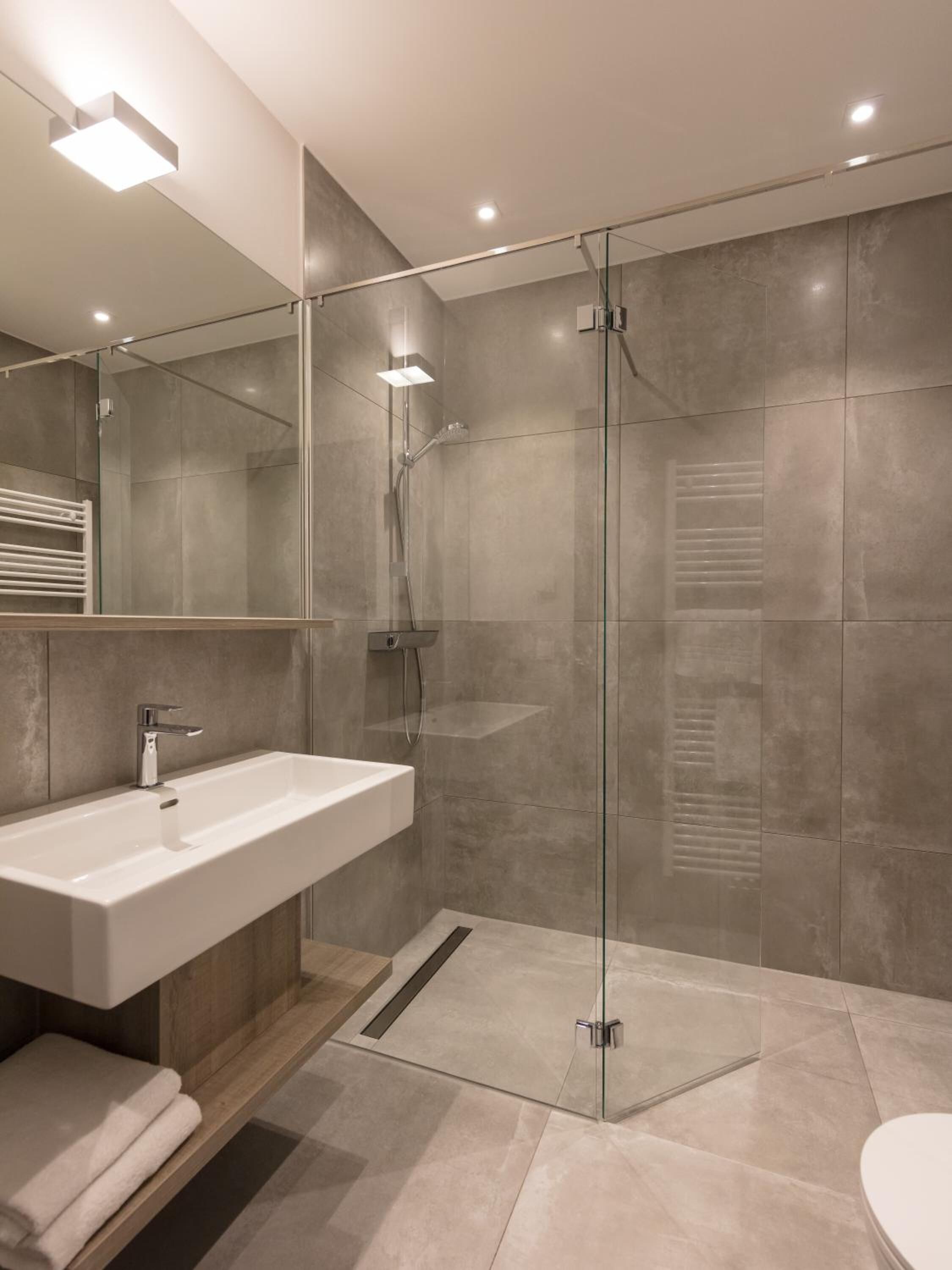 A modern bathroom with a glass-enclosed shower, a white sink, and a wooden shelf.