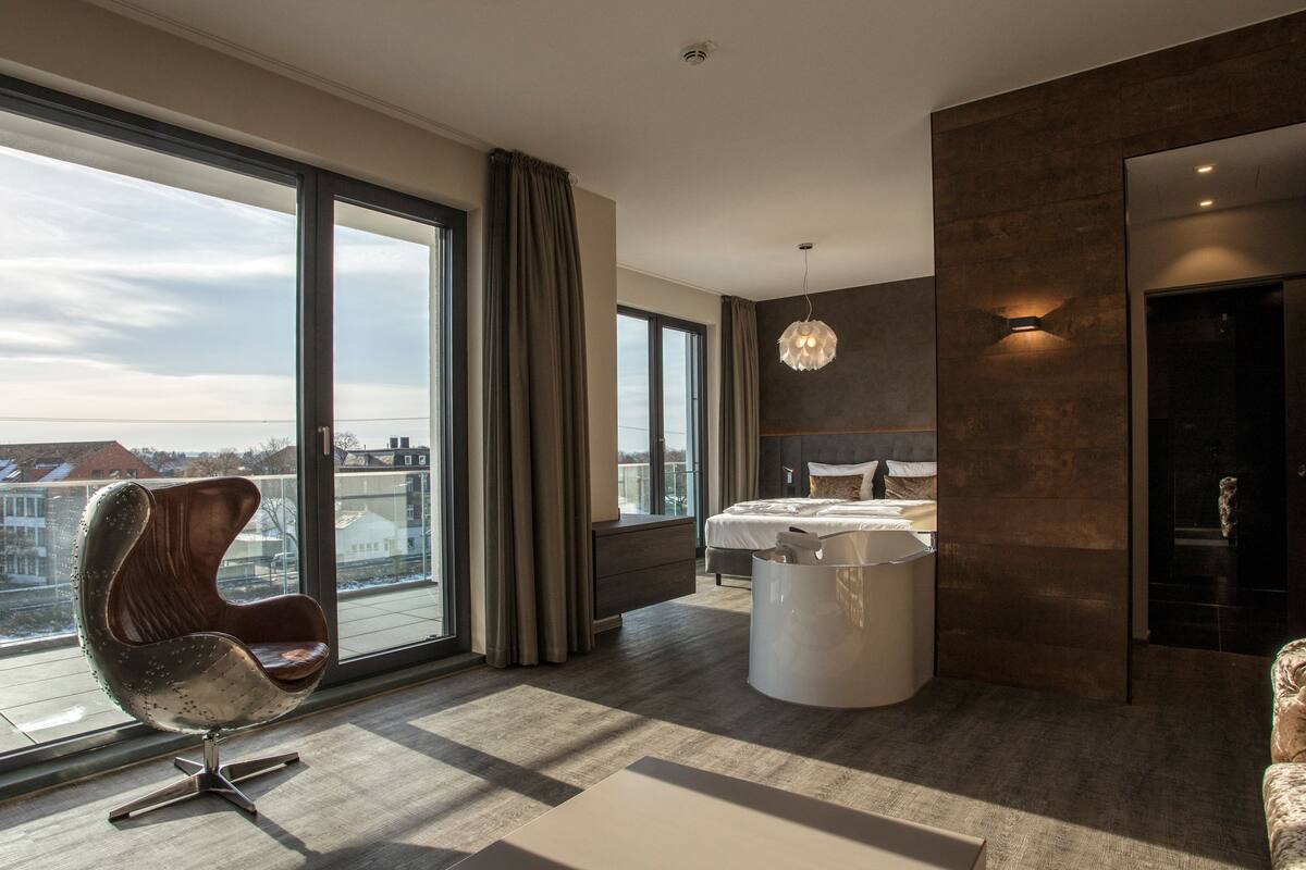 A modern bedroom with a large window, a bed, a chair, and a unique light fixture.