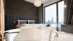 A modern hotel room with a large bed, a bathtub, and a city view through the window. - Deck 8 Designhotel.Soest (Soest)