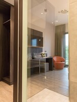 Una habitación moderna y luminosa con un separador de vidrio, un armario de madera, una zona de estar con una silla y vistas a zonas verdes.