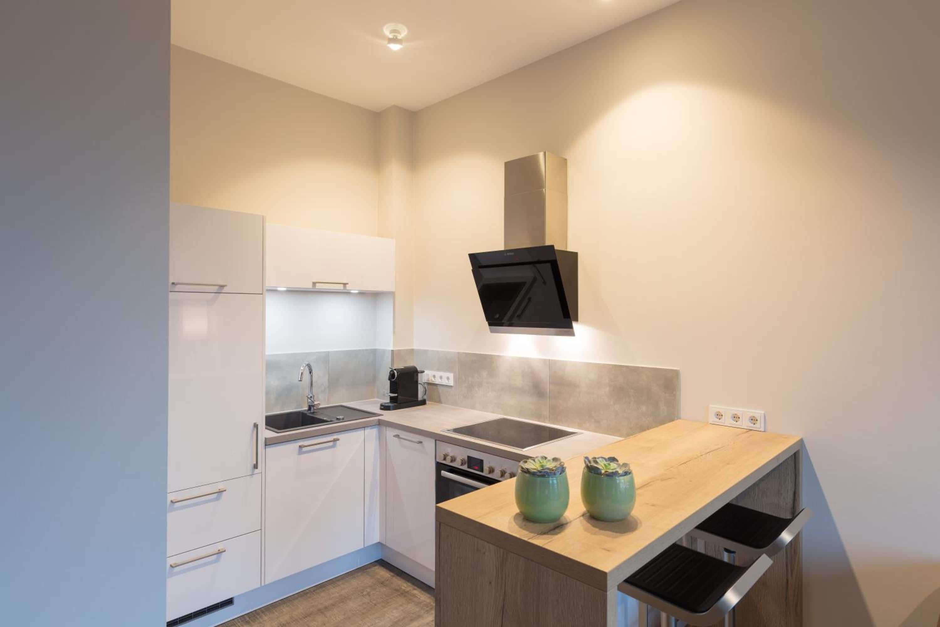 Una cocina moderna con armarios blancos, una campana extractora negra y una encimera de madera con dos jarrones verdes.