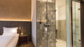 A modern hotel room with a large bed, a glass-enclosed shower, and a nightstand with a lamp.