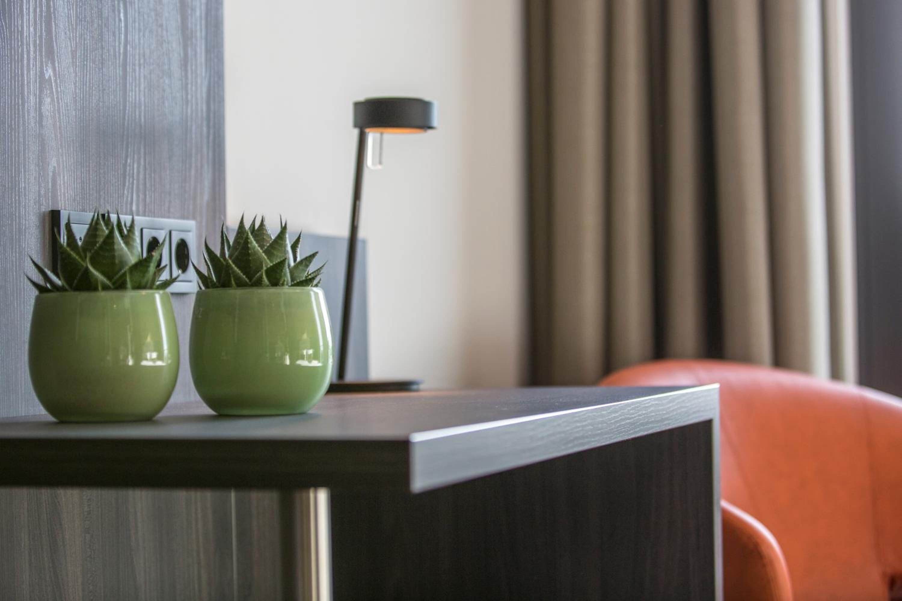 A modern room with a dark wooden desk, two green potted plants, a black floor lamp, and an orange chair.