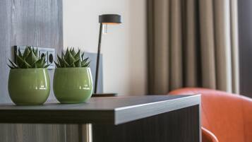 A modern room with a dark wooden desk, two green potted plants, a black floor lamp, and an orange chair.
