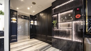 A modern interior with a marble floor, dark wood paneling, and a decorative wall with a plant and a red circular object. - The Grandeur Hotel (Kawasaki)