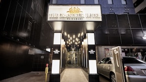 The entrance of The Grandeur Hotel in Kawasaki, featuring a prominent sign, a well-lit pathway, and a parked car. - The Grandeur Hotel (Kawasaki)