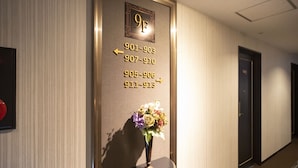 A hotel hallway with a wall-mounted directory listing room numbers and corresponding phone numbers. - The Grandeur Hotel (Kawasaki)