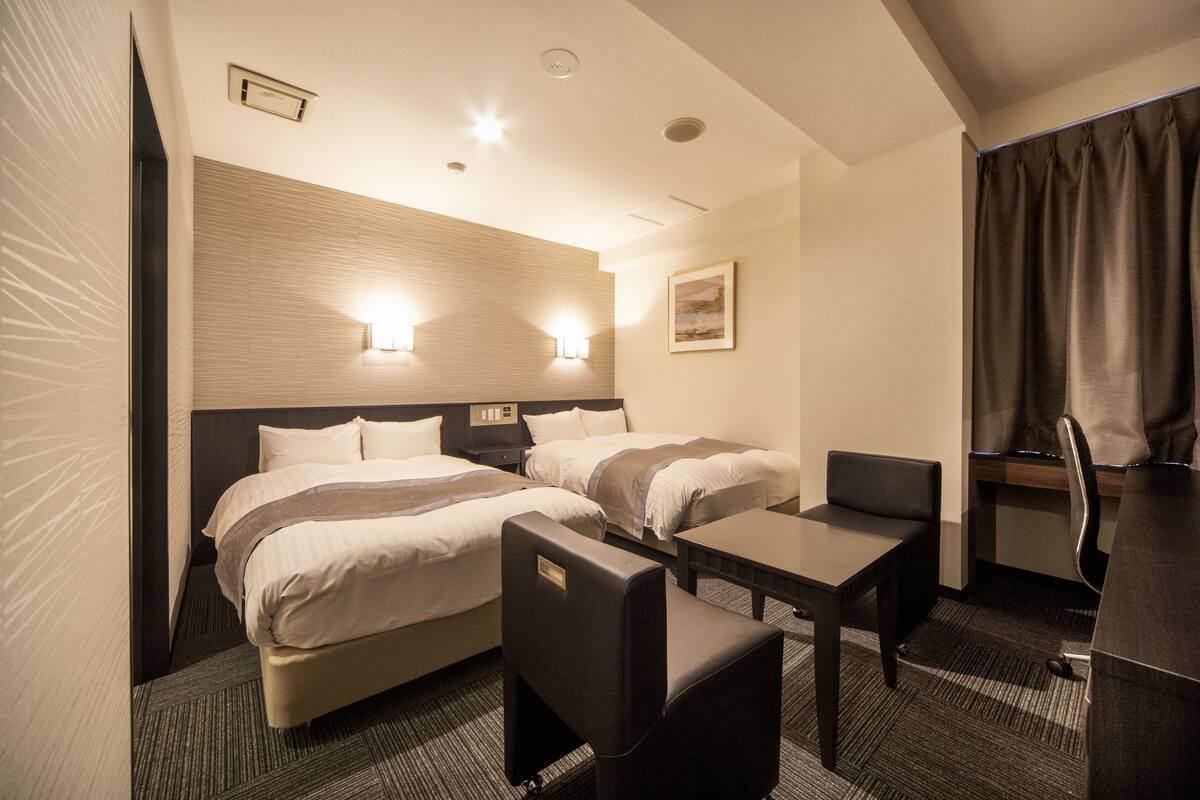 Une chambre d’hôtel avec deux lits, un bureau, une chaise et une petite table.