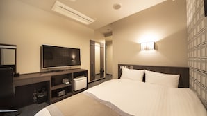 A hotel room with a large bed, a flat-screen TV, a minibar, a desk with a chair, and a wall-mounted light. - The Grandeur Hotel (Kawasaki)