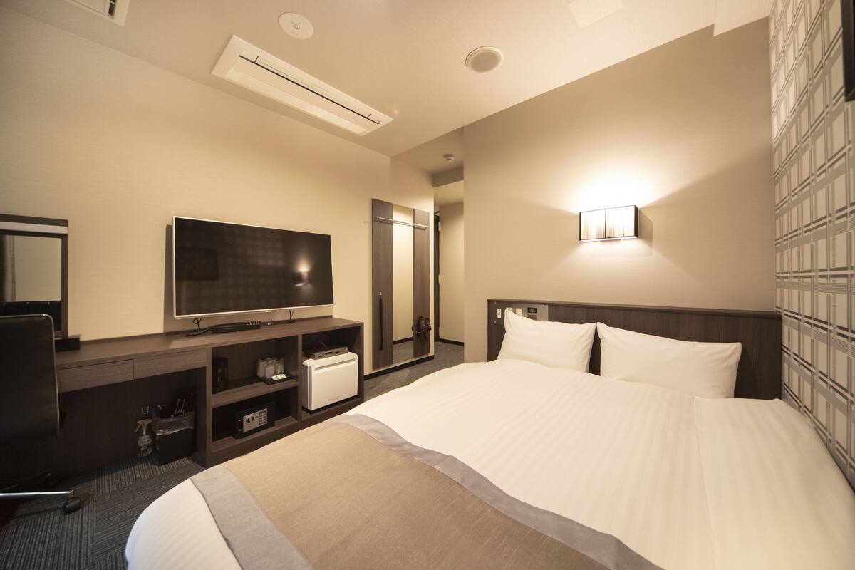 Une chambre d’hôtel dotée d’un grand lit, d’une télévision à écran plat, d’un minibar, d’un bureau avec une chaise et d’une lampe fixée au mur.