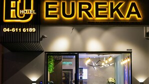 La façade de l'hôtel Eureka, avec son enseigne au néon, son comptoir d'accueil et l'entrée visible d'une chambre.