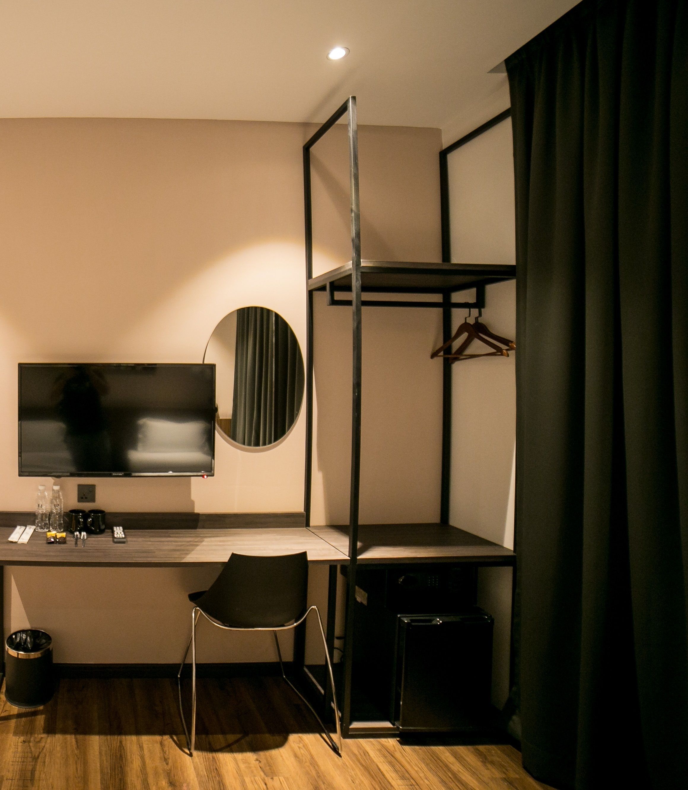 A compact hotel room with a bunk bed, a desk with a flat-screen TV, a chair, a small trash bin, and a mirror.