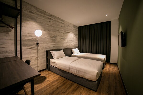 Een moderne hotelkamer met een houten vloer, twee bedden met witte lakens, een bureau, een aan de muur bevestigde televisie en een plafondlamp.