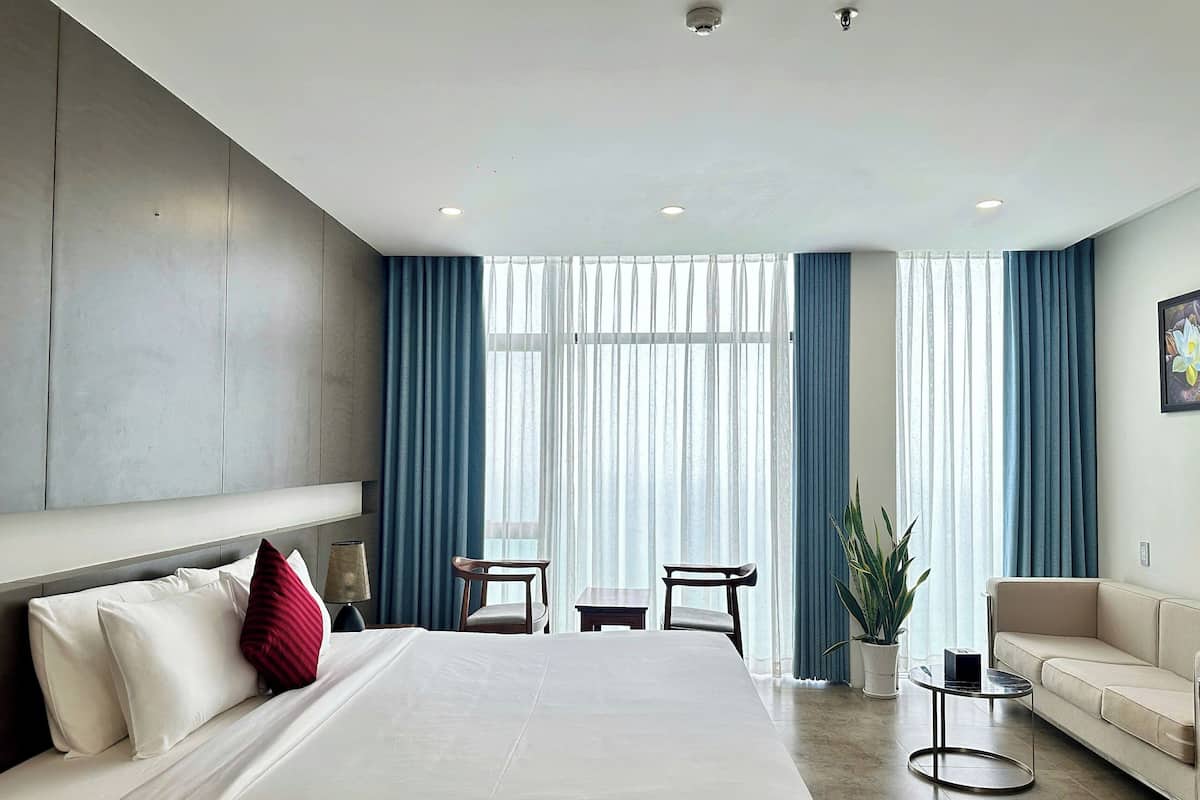 A hotel room with a large bed, a sofa, a small table, and a potted plant.