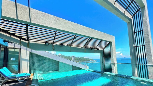 Piscina infinita no terraço, com vista ampla do oceano e montanhas ao longe.