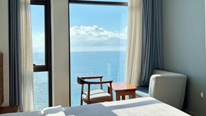 Quarto de hotel com uma janela grande, uma cama, uma cadeira e uma mesa pequena.