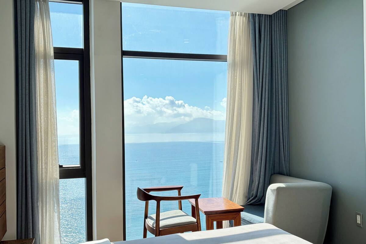 A hotel room with a large window, a bed, a chair, and a small table.