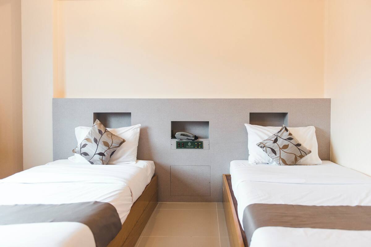A hotel room with two single beds, each with a pillow and a bedside table.