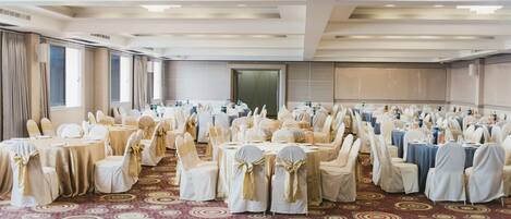 A banquet hall with round tables and chairs, a patterned carpet, and a large mirror on the wall.