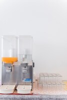 A beverage dispenser with two push buttons and a stack of clear glasses on a patterned tablecloth.