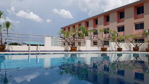A swimming pool with clear water reflecting the sky and surrounding buildings. There are potted plants along the poolside. - K.S. Pavilion Hotel (Nakhon Ratchasima)