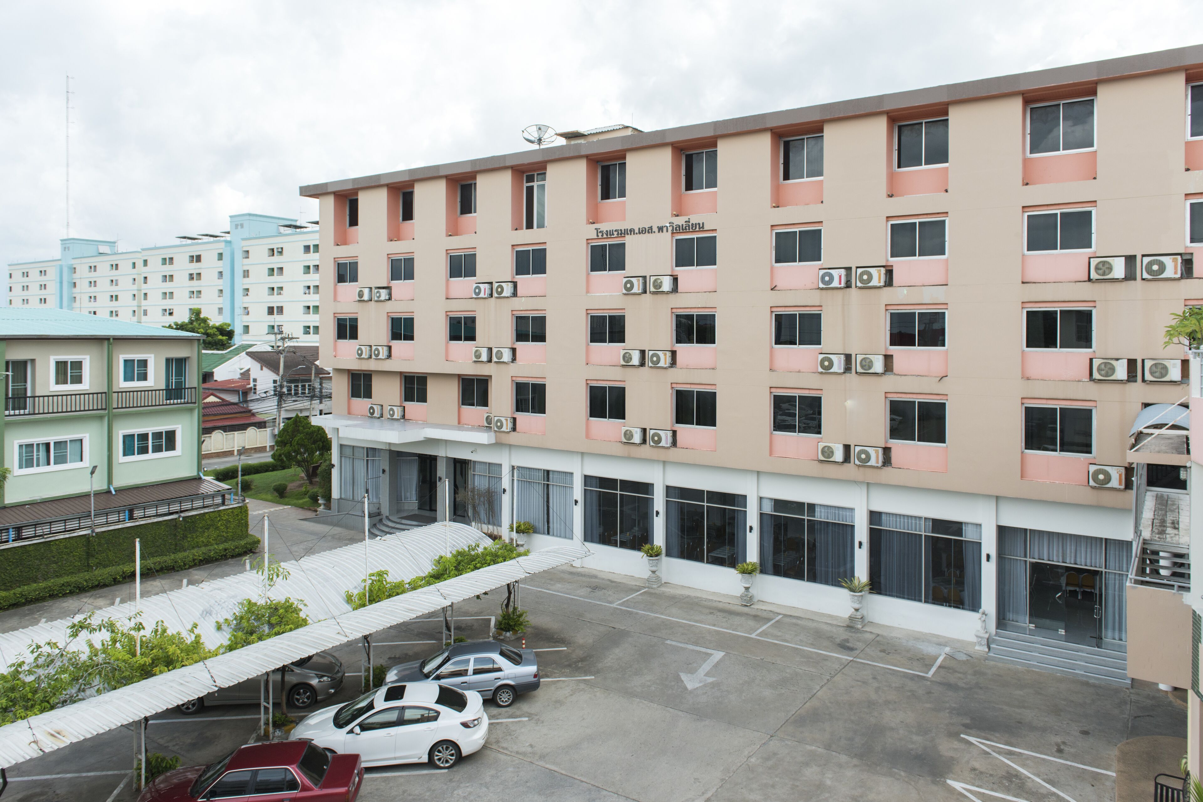 A multi-story hotel with a row of air conditioning units, a covered parking area, and a clear view of the surrounding buildings.