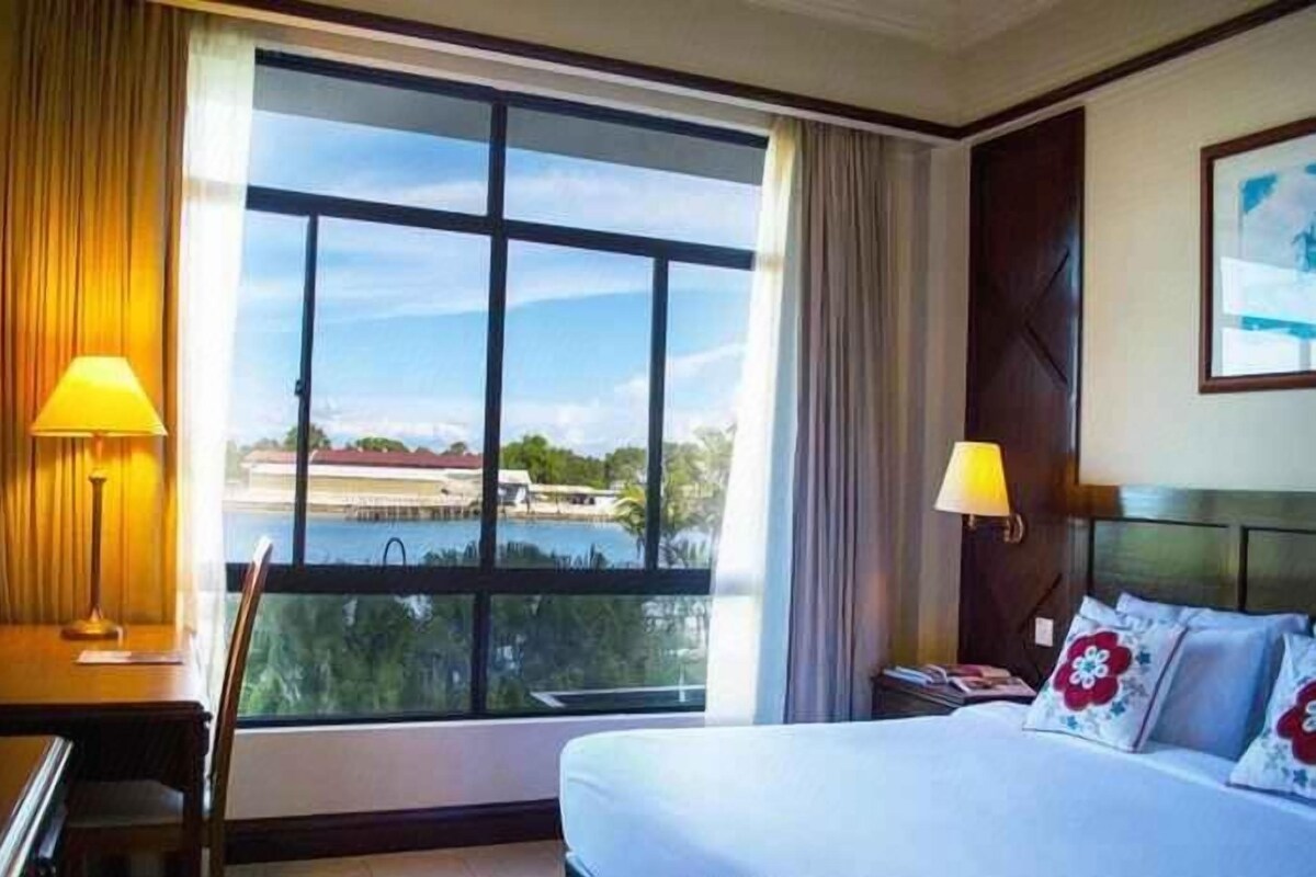 A hotel room with a large window, a bed, two bedside tables, and a view of a body of water.
