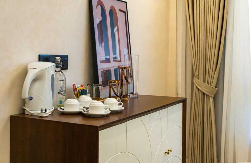 A hotel room with a coffee station, a framed picture on the wall, and a curtain.