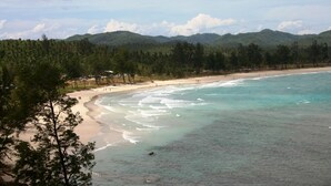A beach with clear turquoise waters, sandy shore, and a backdrop of green hills.