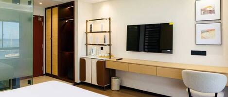 A hotel room with a bed, a desk, a chair, a TV, a wardrobe, and a small trash bin.