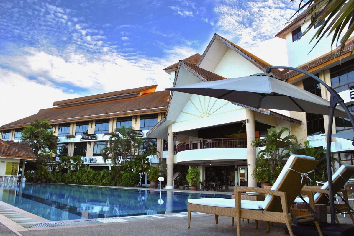 A hotel with a swimming pool, lounge chairs, and a covered area with umbrellas.