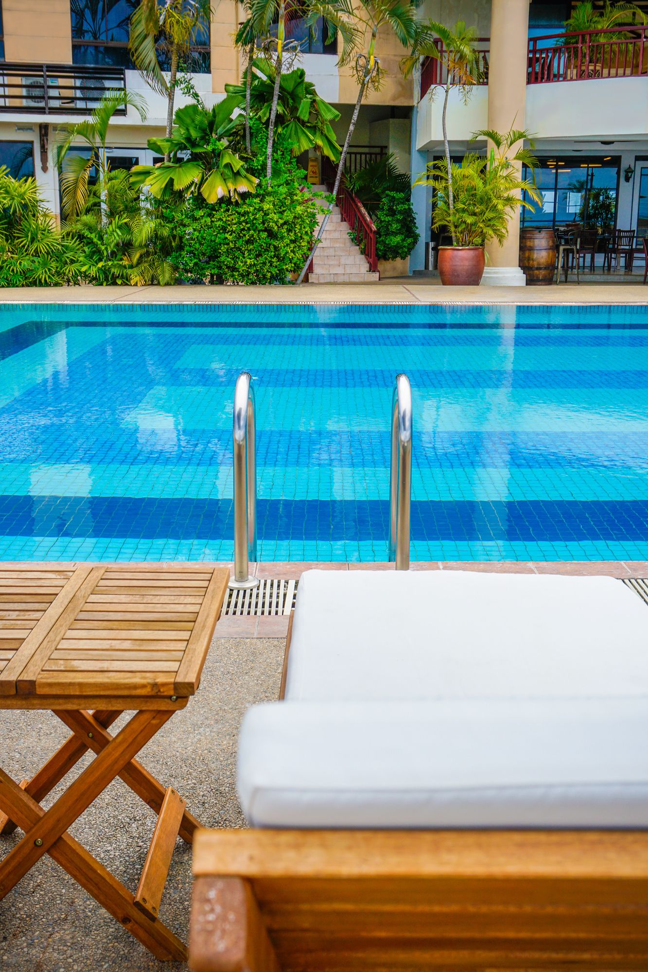 Zona de piscina con una piscina azul cristalina, sillones de madera y exuberante vegetación.