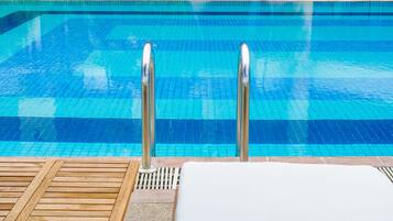 Zona de piscina con una piscina azul cristalina, sillones de madera y exuberante vegetación.