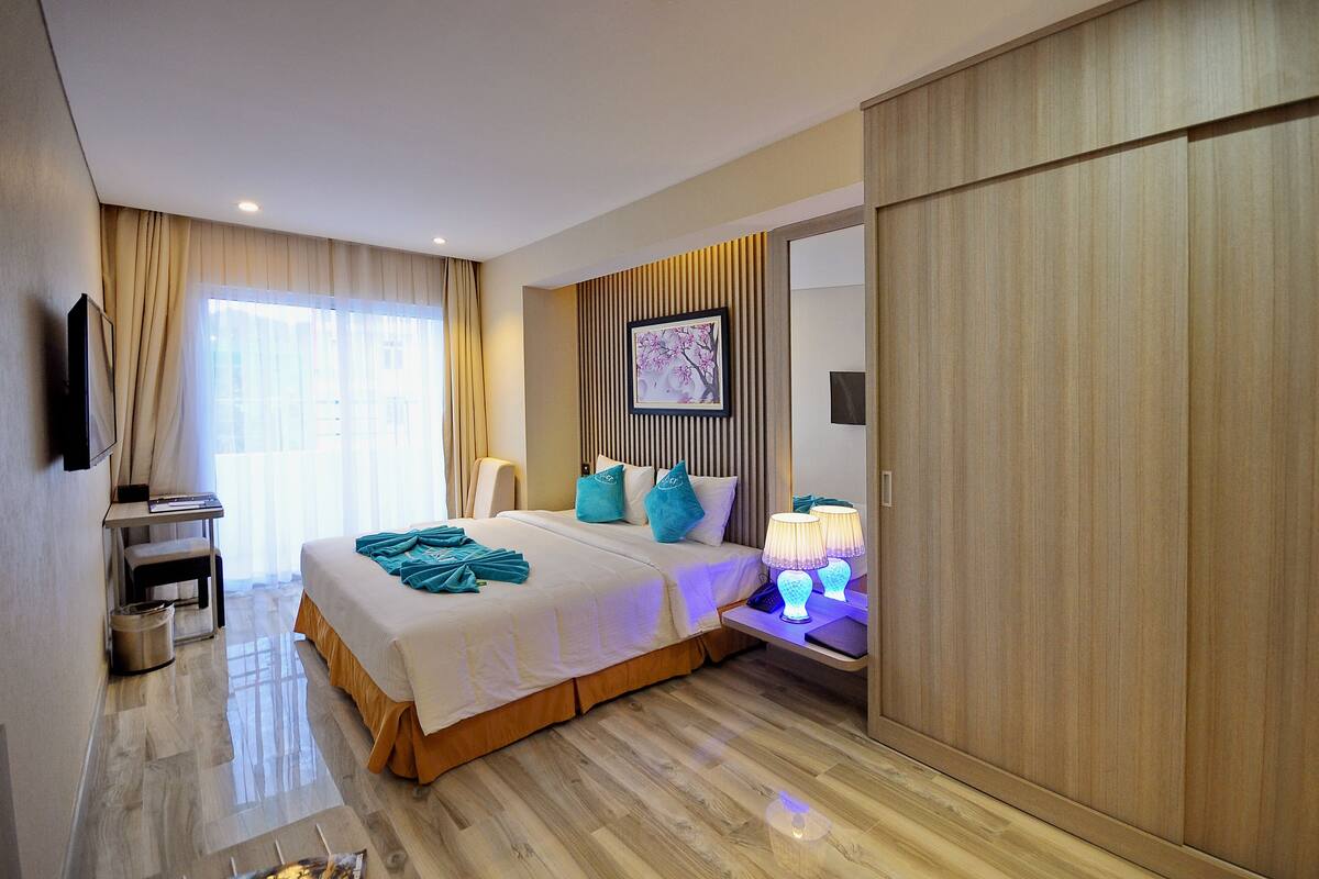 Una habitación de hotel con cama, mesita de noche, lámpara y un espejo grande.