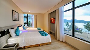 Une chambre d’hôtel avec deux lits, une grande fenêtre donnant sur la plage et un tableau encadré au mur.