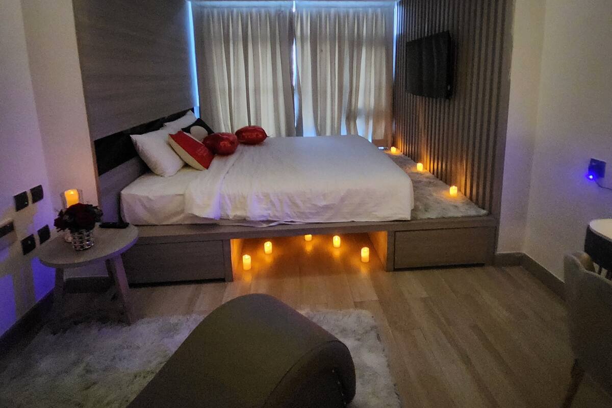 Un dormitorio moderno con cama, mesita de noche y una pequeña zona de estar.