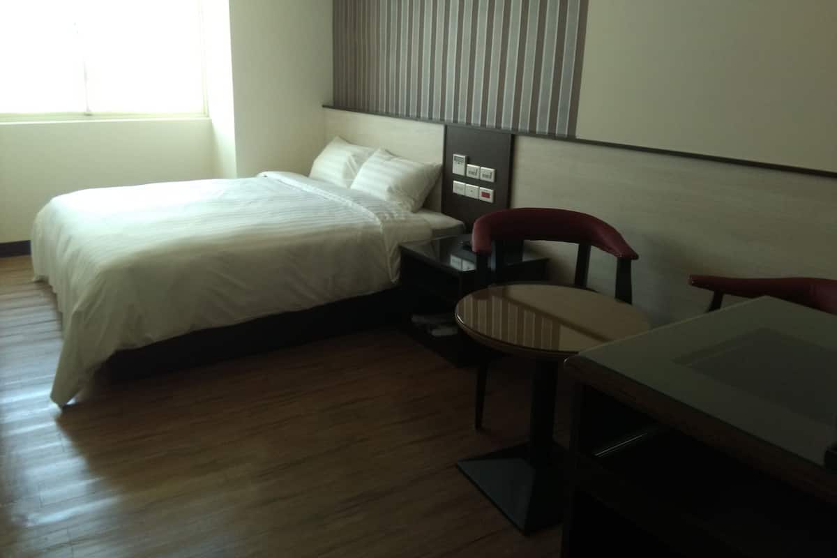 A hotel room with a bed, a desk, a chair, and a control panel on the wall.