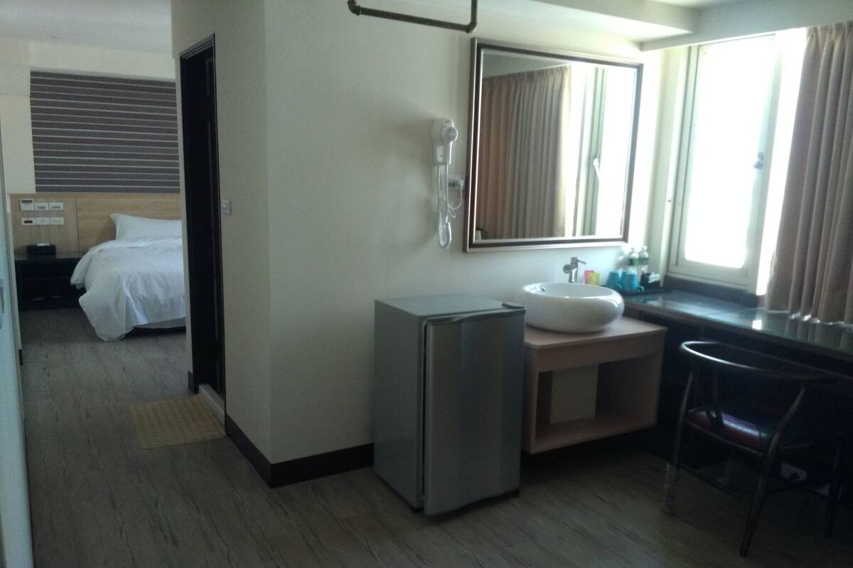 A hotel room with a bed, a small refrigerator, a sink, and a mirror.