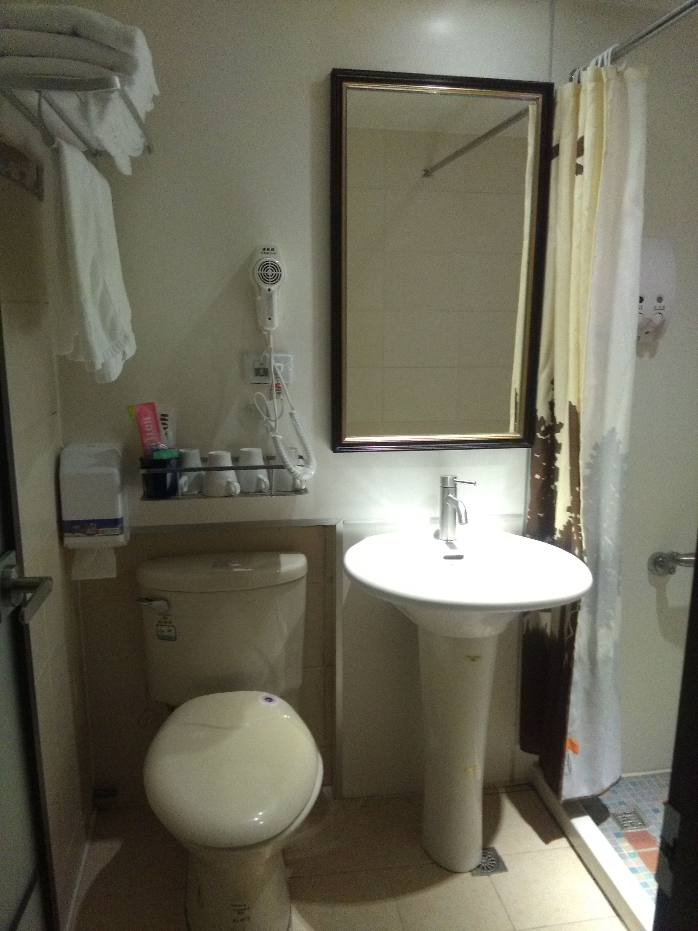 Un baño con inodoro, lavamanos y un secador de pelo en la pared.