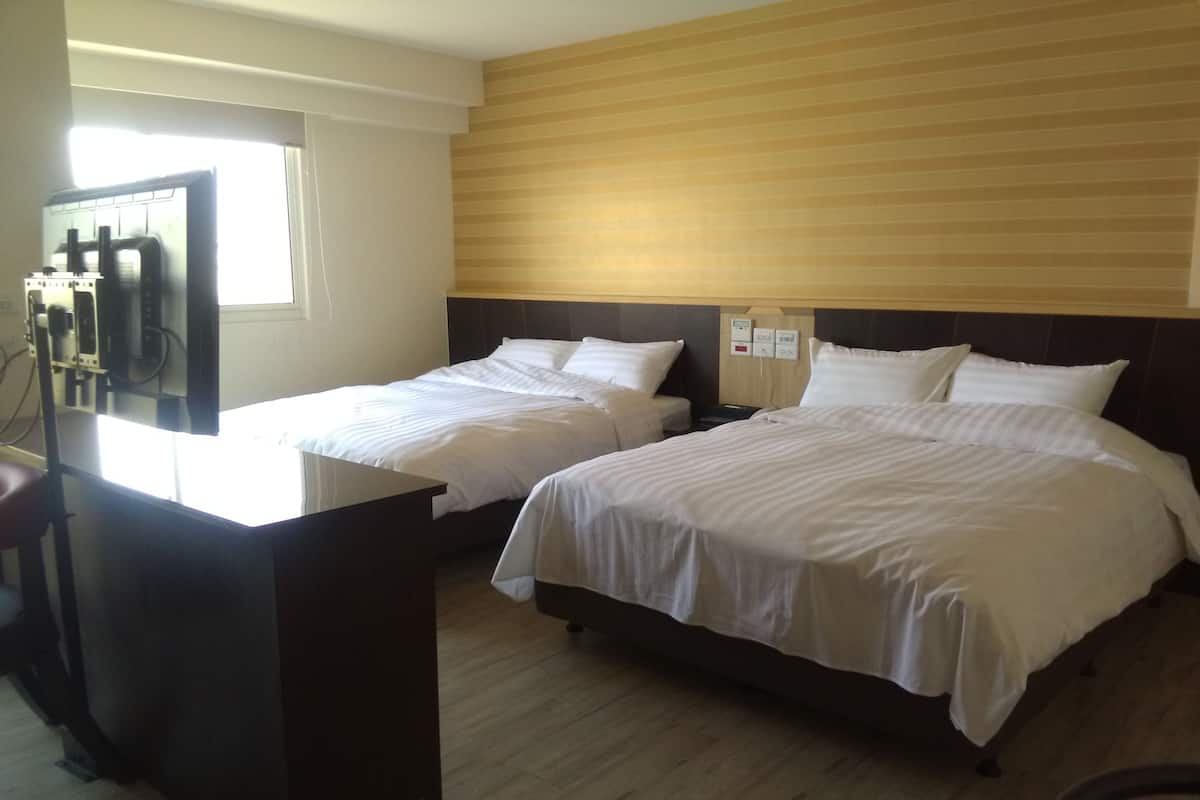 A hotel room with two beds, a wooden headboard, a desk, and a window with blinds.