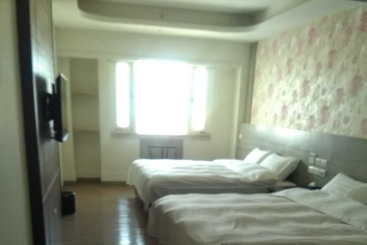 A hotel room with two beds, a small refrigerator, and a window with blinds.