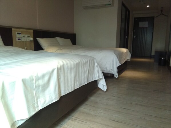 Habitación de hotel con dos camas, piso de madera y una puerta que da a otra habitación.